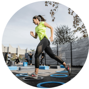Woman wearing green shirt and black leggings running on circles with people in background